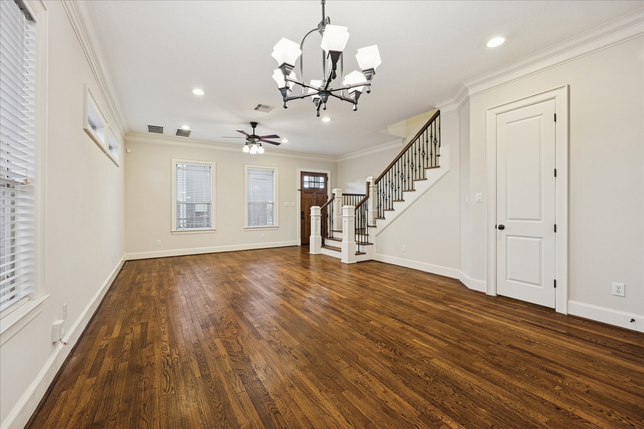 840 Alexander Street Houston, TX 77007 - Photo 11 of 39 This spacious, open-concept living area with hardwood floors, ample natural light from multiple windows, and elegant fixtures including a ceiling fan and chandelier. This space can be used as a formal entry, living and dining room. The staircase leading upstairs to all bedrooms, including the primary suite. Pictured on the right is a large under staircase storage. Just to the right is a historic styled half bath.