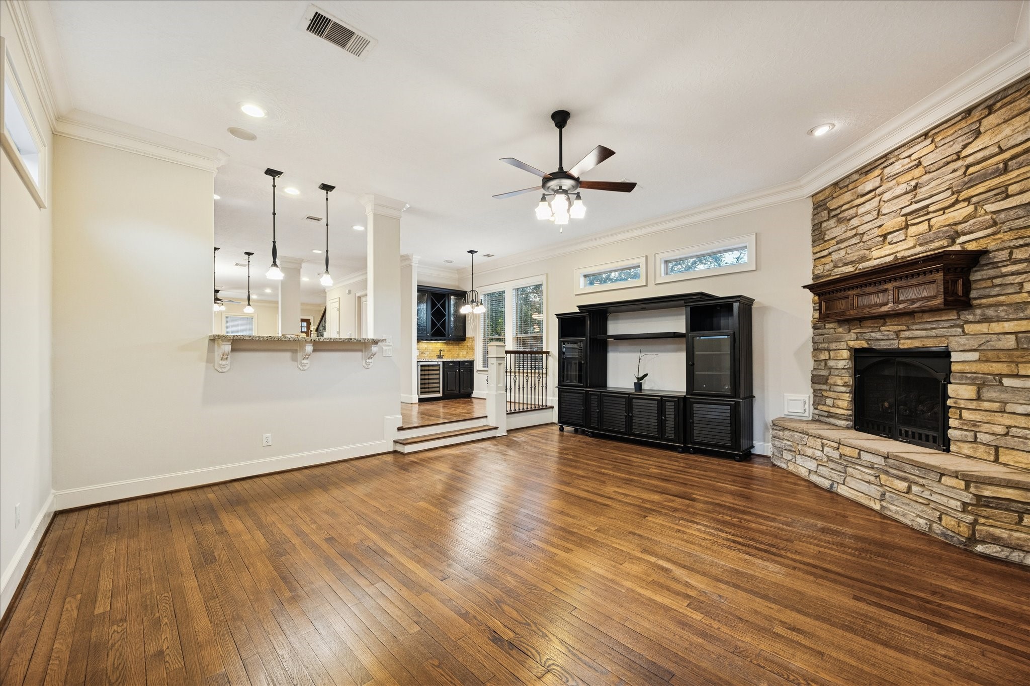 840 Alexander Street Houston, TX 77007 - Photo 13 of 39 This inviting living room features warm hardwood floors, a striking stone fireplace, and ample natural light from high windows. It opens to a modern kitchen with a breakfast bar and pendant lighting, creating a seamless space for entertaining. Access the garage, side yard and garage apartment through the French doors at the back of this room.