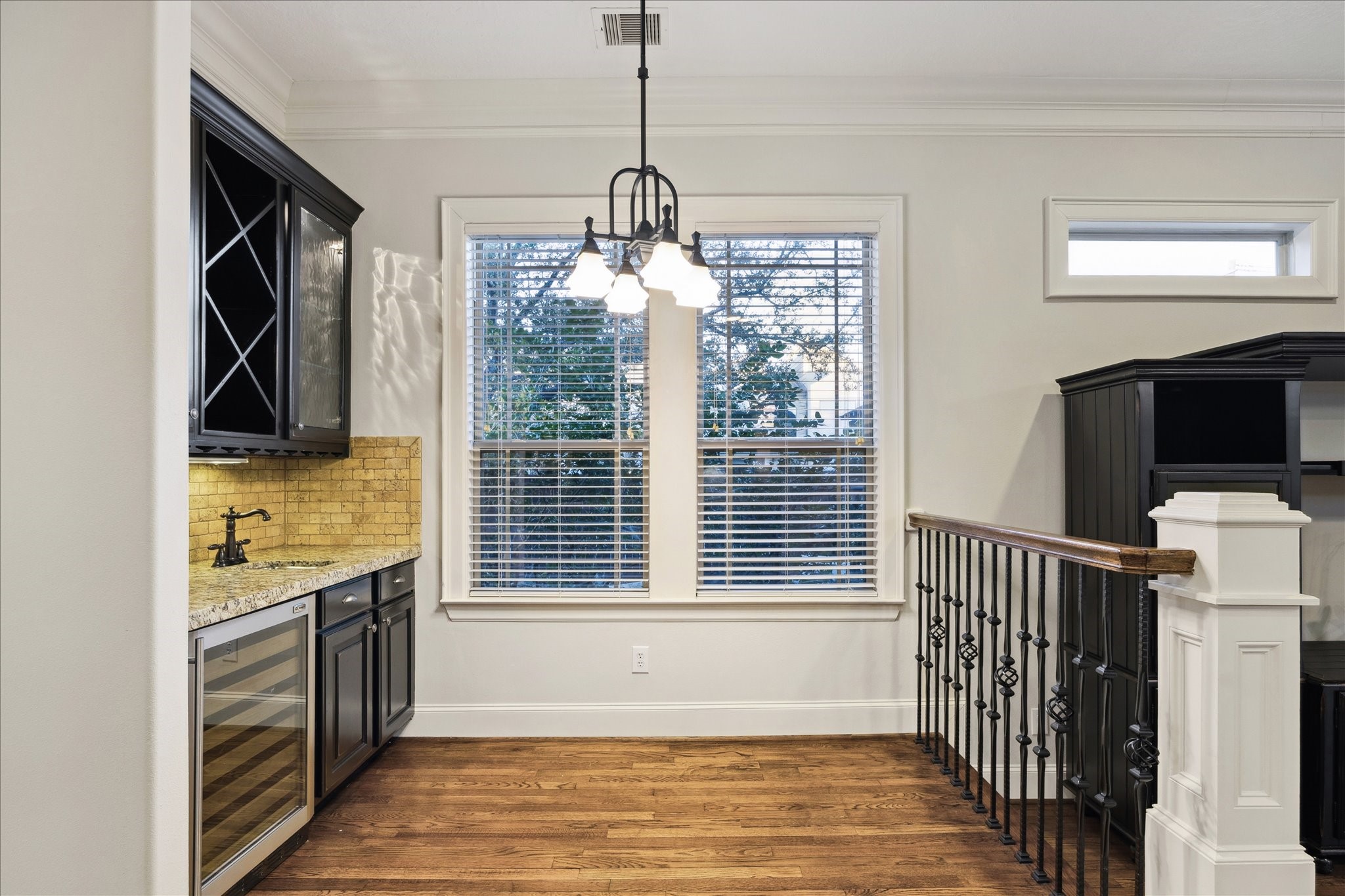 840 Alexander Street Houston, TX 77007 - Photo 16 of 39 This photo showcases a bright, elegant bar area with hardwood floors with stylish iron railing. Featuring matching custom cabinetry with glass doors, a granite countertop, and a GE wine cooler. Large windows with blinds allow natural light to fill the space, with views of the Satsuma tree and hot tub that is included with this home.