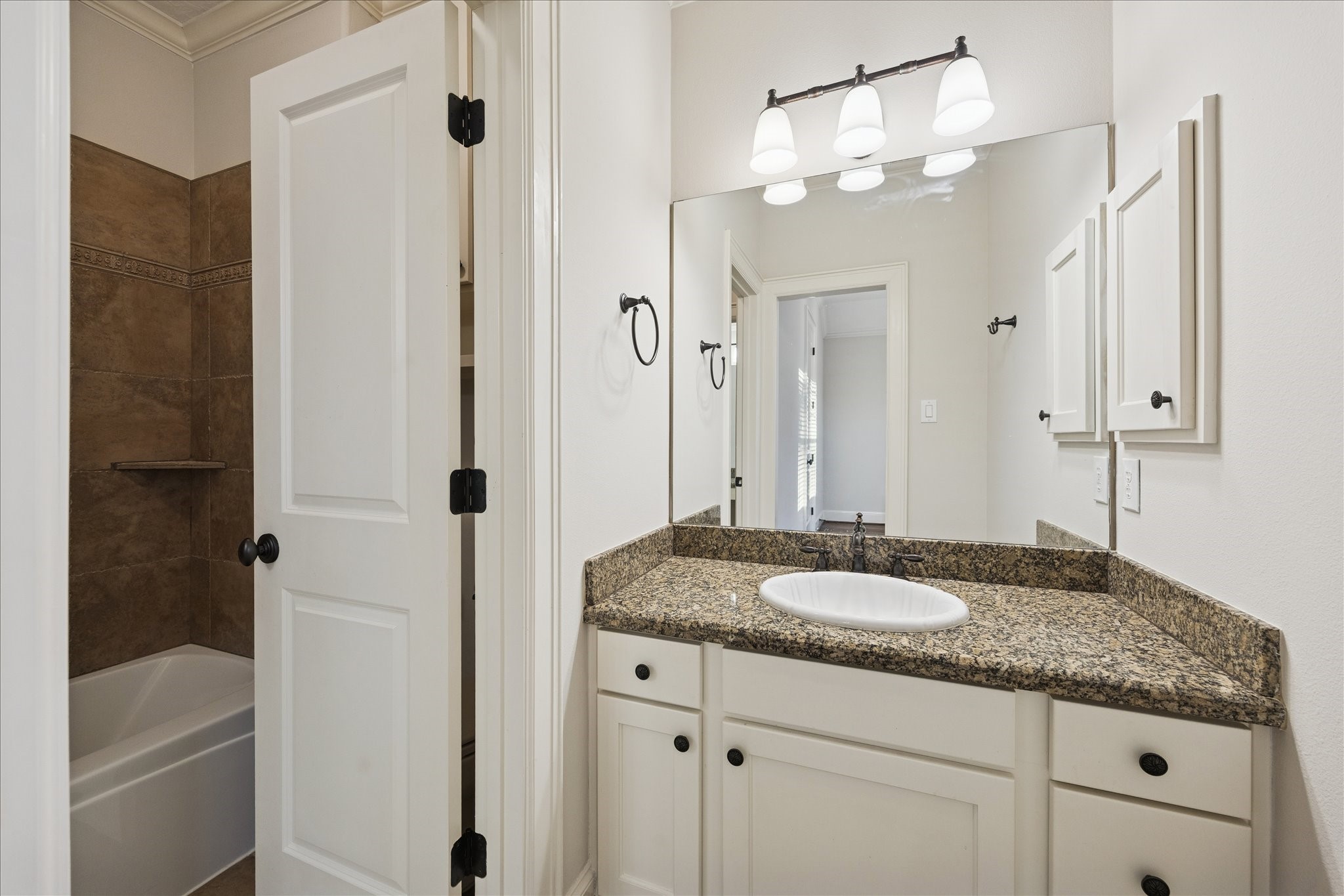 840 Alexander Street Houston, TX 77007 - Photo 22 of 39 This secondary bathroom features a granite countertop with an under-mount sink, sleek fixtures, and ample cabinet storage. It has a large mirror with modern lighting and an adjoining bathtub with a tiled shower area.