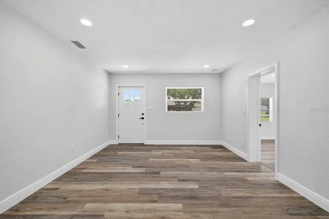 a view of an empty room with wooden floor and window