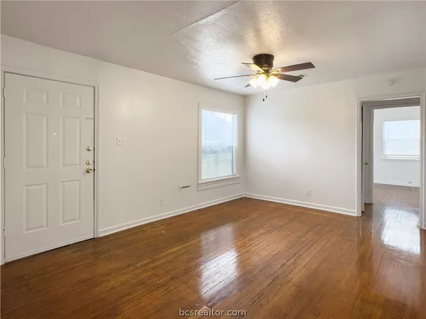 a view of an empty room with wooden floor and a ceiling fan