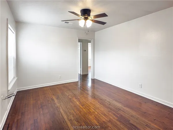 a view of an empty room with wooden floor and a ceiling fan