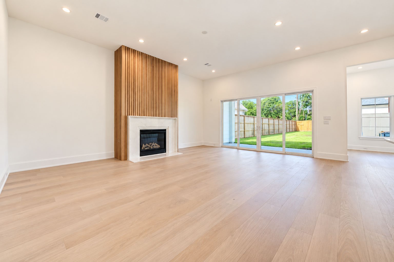 2309 Hollister Road Houston, TX 77080 - Photo 5 of 47 Sun-drenched living space showcases clean architectural lines, wide-plank flooring, and a dramatic floor-to-ceiling fireplace framed by warm wood accents. Expansive windows invite views of the backyard while filling the room with natural light, creating a sophisticated yet inviting setting for relaxed evenings, elegant entertaining, and seamless indoor-outdoor living.
