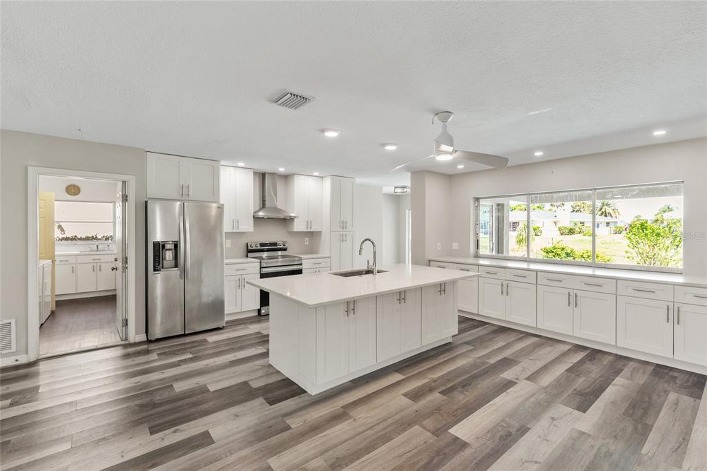 1009 Kings Court Venice, FL 34293 - Photo 2 of 25 a large white kitchen with a refrigerator a sink dishwasher a stove and white cabinets with wooden floor