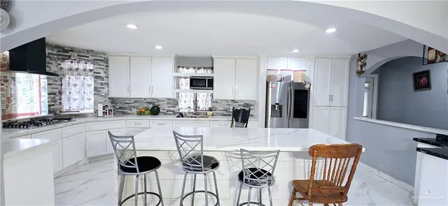 a kitchen with stainless steel appliances kitchen island granite countertop a refrigerator a stove a sink dishwasher with a dining table and chairs with wooden floor