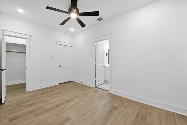 a view of an empty room with wooden floor and a ceiling fan