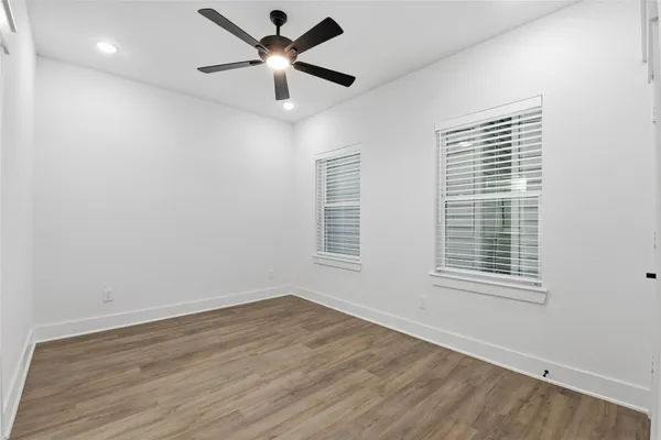 a view of an empty room with wooden floor and a ceiling fan