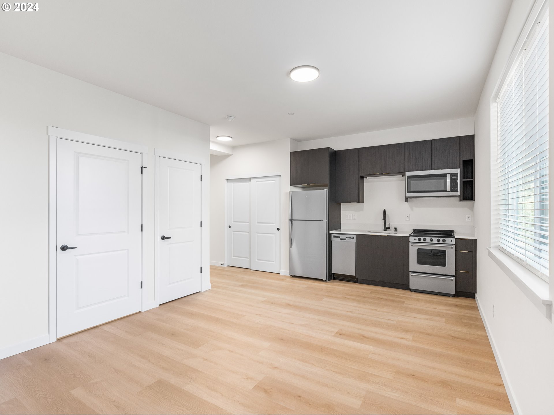 10985 East Burnside Street, Unit 1 Portland, OR 97216 - Photo 4 of 7 a large white kitchen with stainless steel appliances kitchen island a sink dishwasher a stove and a refrigerator with wooden floor