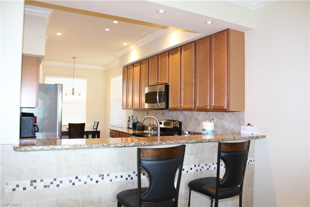 9735 Acqua Court, Unit 611 Naples, FL 34113 - Photo 6 of 30 Kitchen featuring ornamental molding, tasteful backsplash, light stone counters, decorative light fixtures, and brown cabinetry