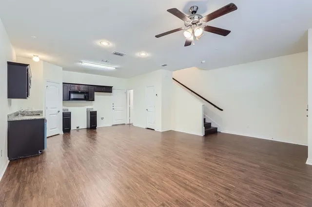 a view of an empty room with a kitchen and a ceiling fan