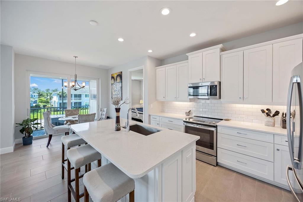 2603 Seychelles Circle, Unit 1505 Naples, FL 34112 - Photo 13 of 35 a kitchen with stainless steel appliances a table chairs refrigerator and cabinets