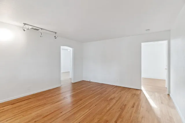 a view of an empty room with wooden floor and a ceiling fan
