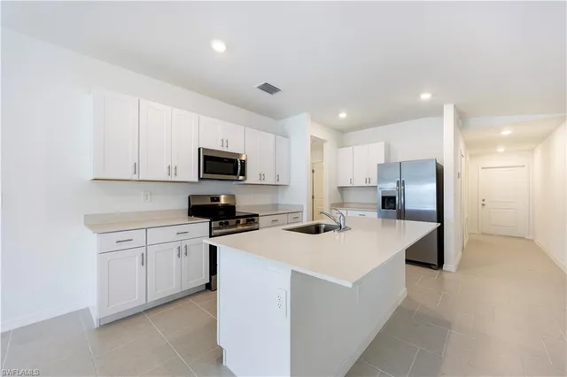 a kitchen that has a lot of white cabinets and stainless steel appliances