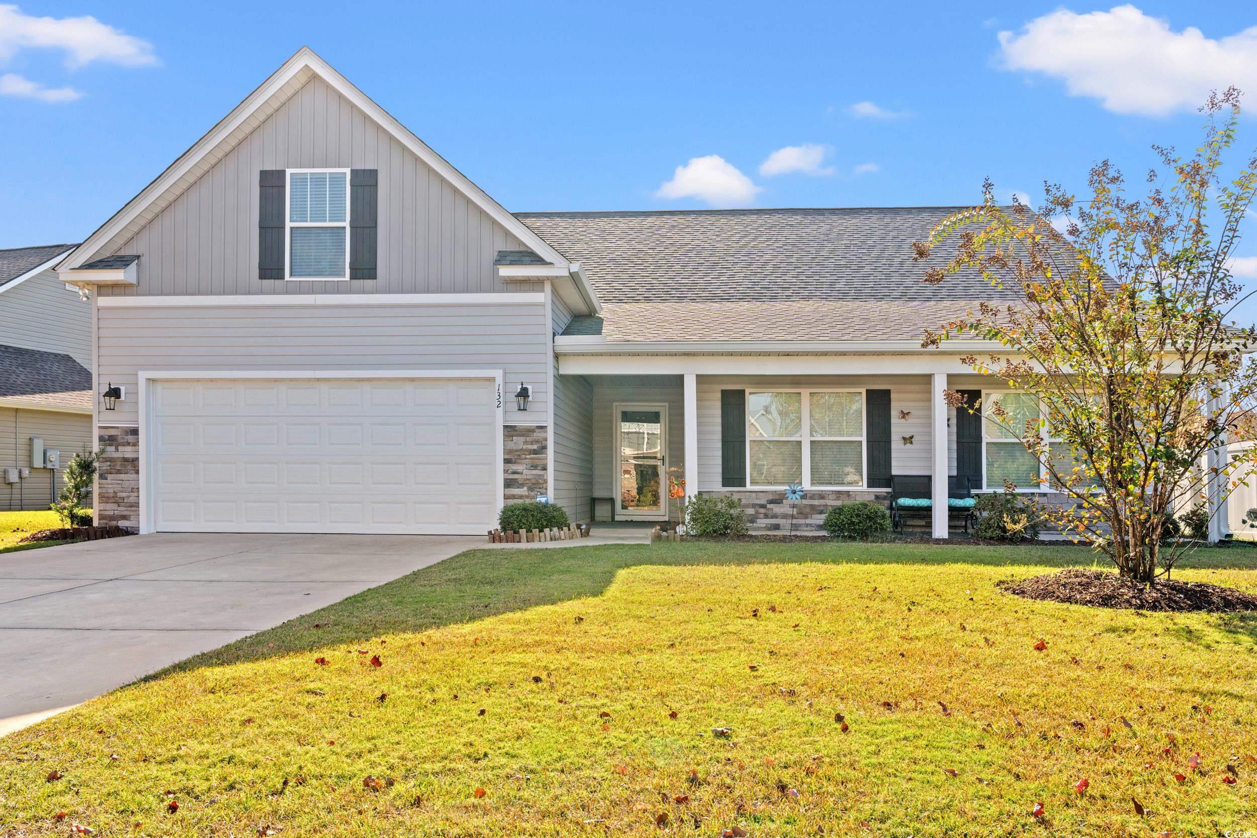 View of front of home featuring covered porch, a front lawn, stone siding, concrete driveway, and roof with shingles
