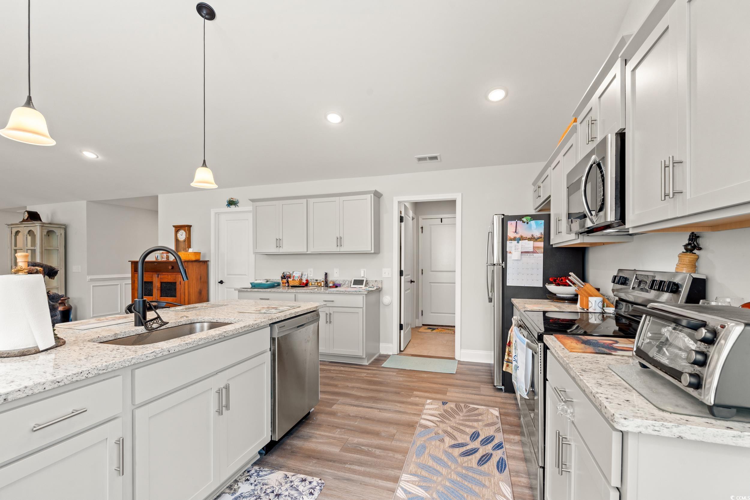 132 Fox Den Drive Murrells Inlet, SC 29576 - Photo 8 of 35 Kitchen with appliances with stainless steel finishes, white cabinets, light stone counters, decorative light fixtures, and light wood finished floors