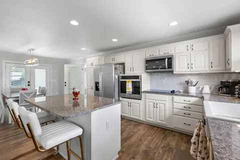 a kitchen with stainless steel appliances granite countertop a sink dishwasher a stove a refrigerator a microwave oven with white cabinets and wooden floor