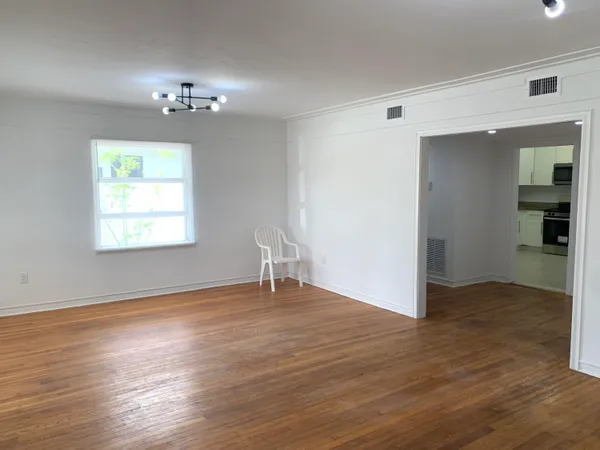 an empty room with wooden floor chandelier and windows