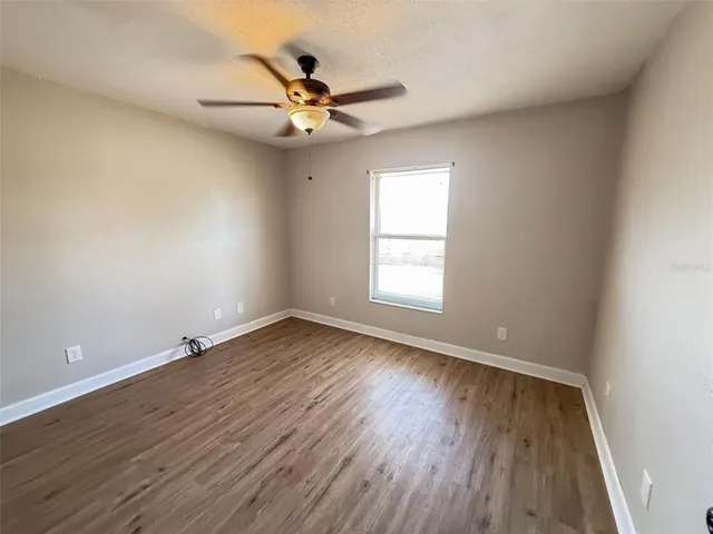 an empty room with wooden floor fan and windows