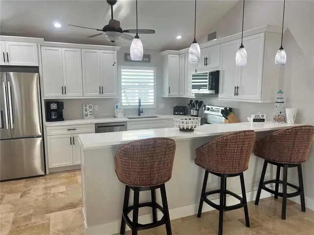 a kitchen with stainless steel appliances granite countertop a sink a stove a refrigerator cabinets and chairs