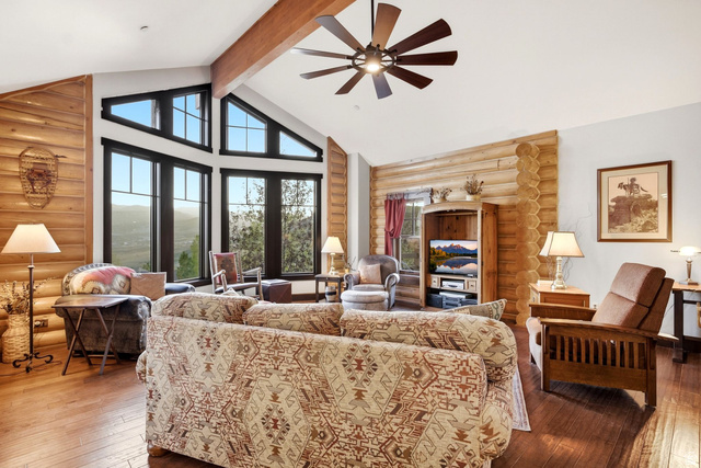12465 Bone Road Kamas, UT 84036 - Photo 14 of 63 Vaulted ceiling with exposed wood beam, wood-finish flooring, custom log wall accents, multi-pane picture windows, and a ceiling fan