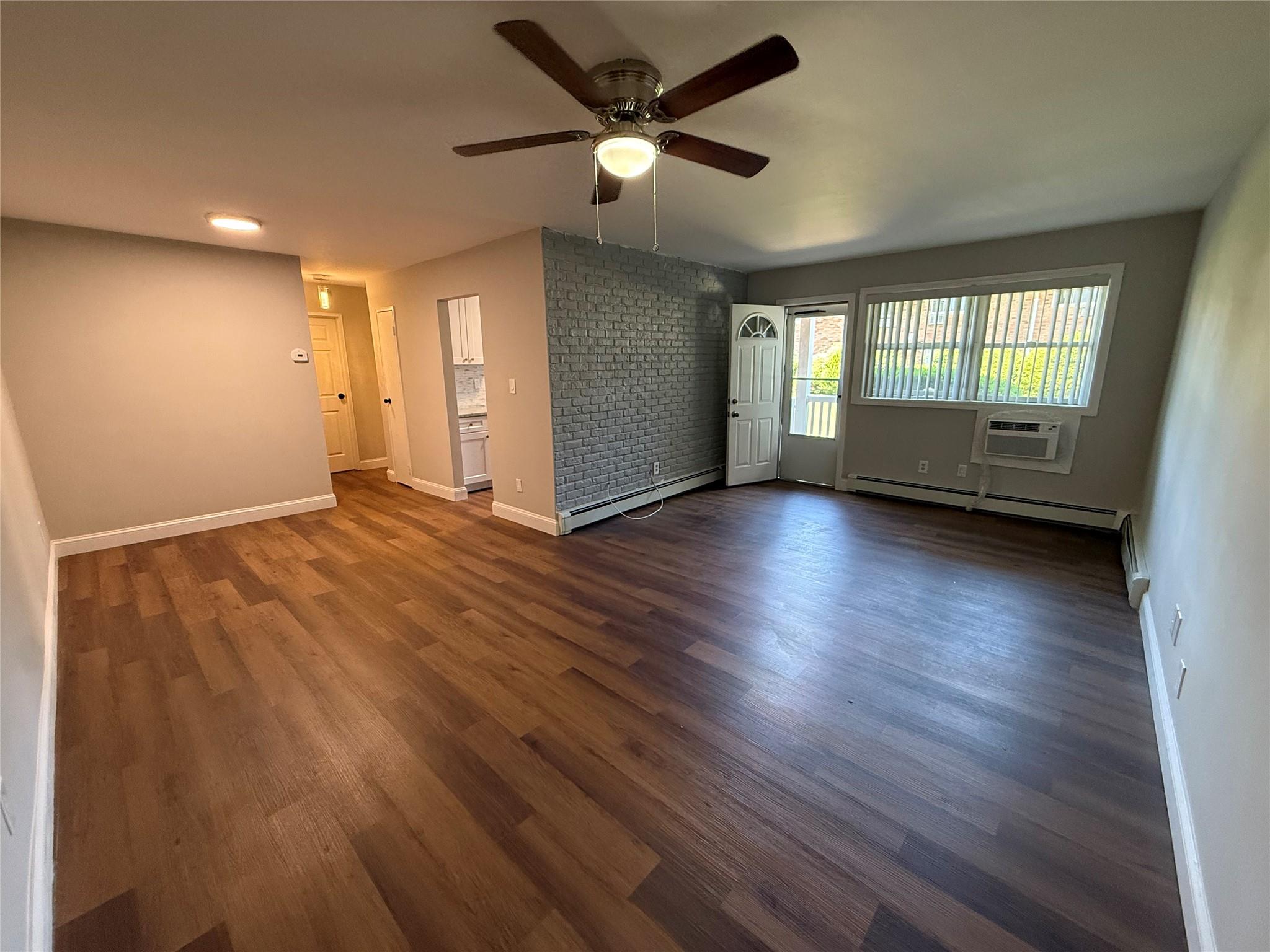 77 Adams Road, Unit 1D Central Islip, NY 11722 - Photo 1 of 1 Spare room featuring a ceiling fan, an AC wall unit, a baseboard heating unit, and dark wood-style flooring