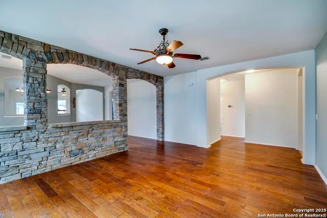 a view of an empty room with chandelier fan and wooden floor