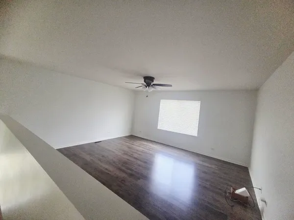 an empty room with wooden floor ceiling fan and windows
