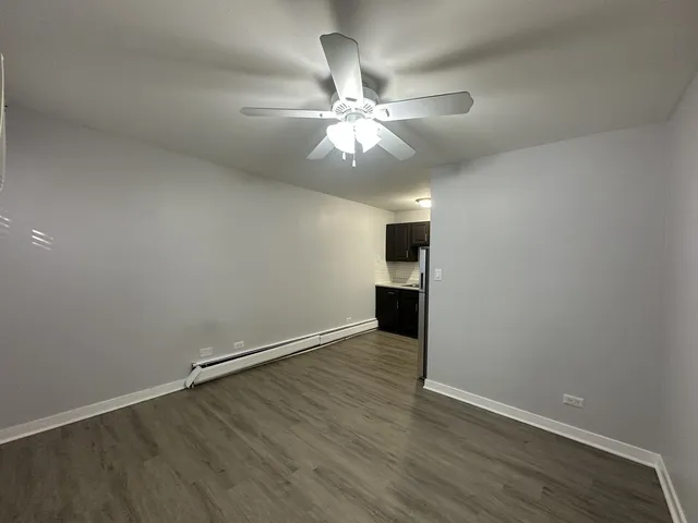 an empty room with wooden floor a ceiling fan and kitchen view