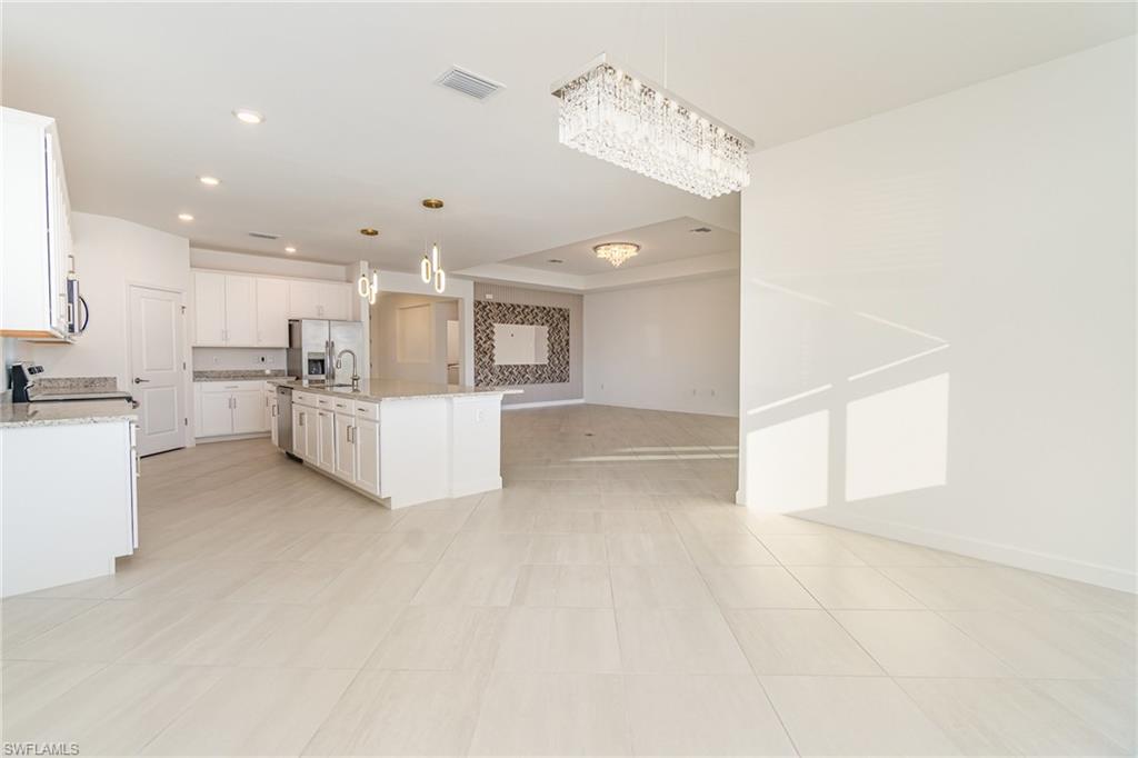 11127 Canopy Loop Fort Myers, FL 33913 - Photo 5 of 29 Kitchen featuring light stone counters, open floor plan, white cabinetry, a center island with sink, and stainless steel refrigerator with ice dispenser