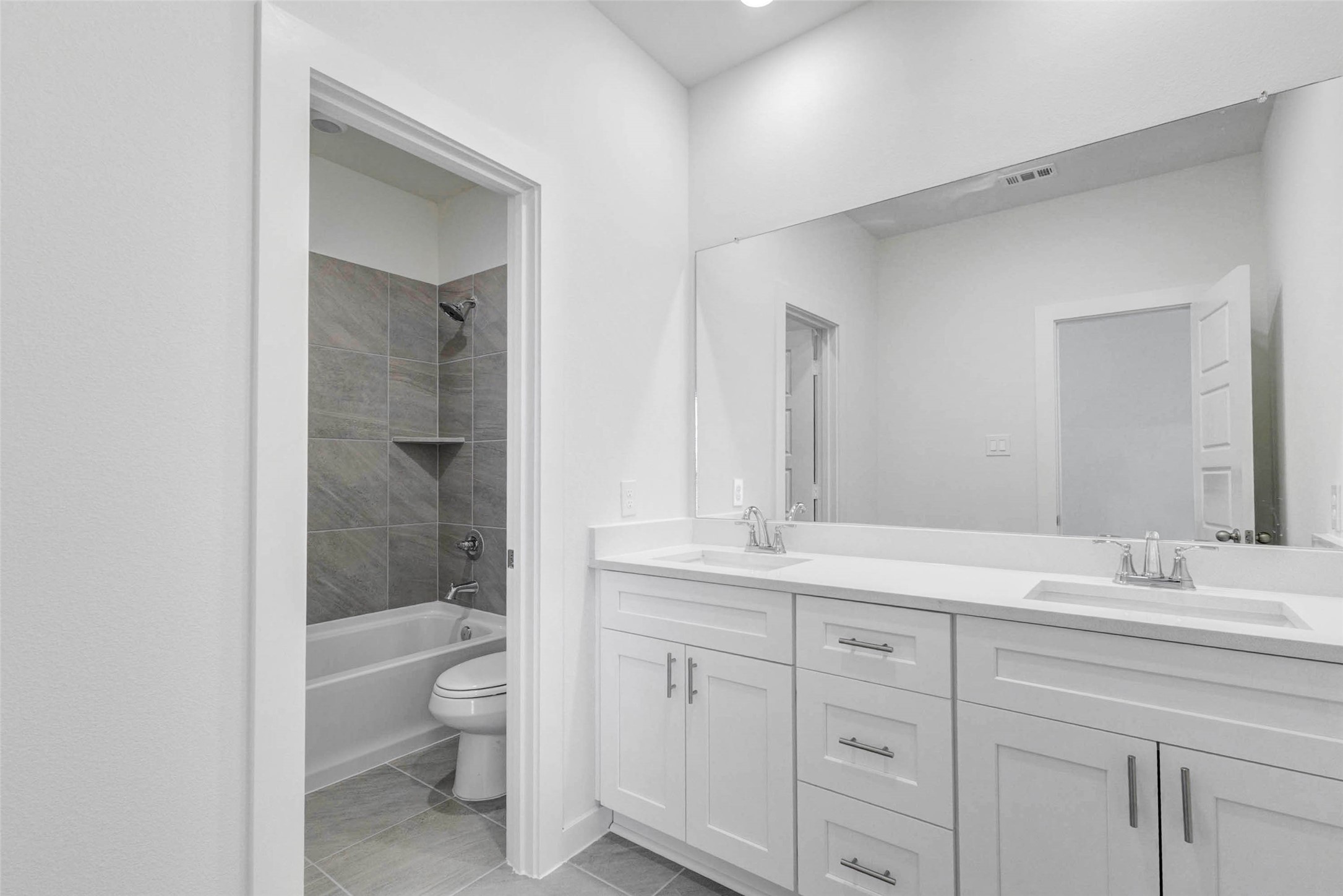6471 Escondido Drive Rosharon, TX 77583 - Photo 29 of 33 Secondary bath vanity area with dual sinks, white cabinetry, quartz-style countertop, large mirror, and nearby tub/shower room. The layout provides everyday convenience for shared use, while the neutral finishes and clean lines keep the space bright and functional.