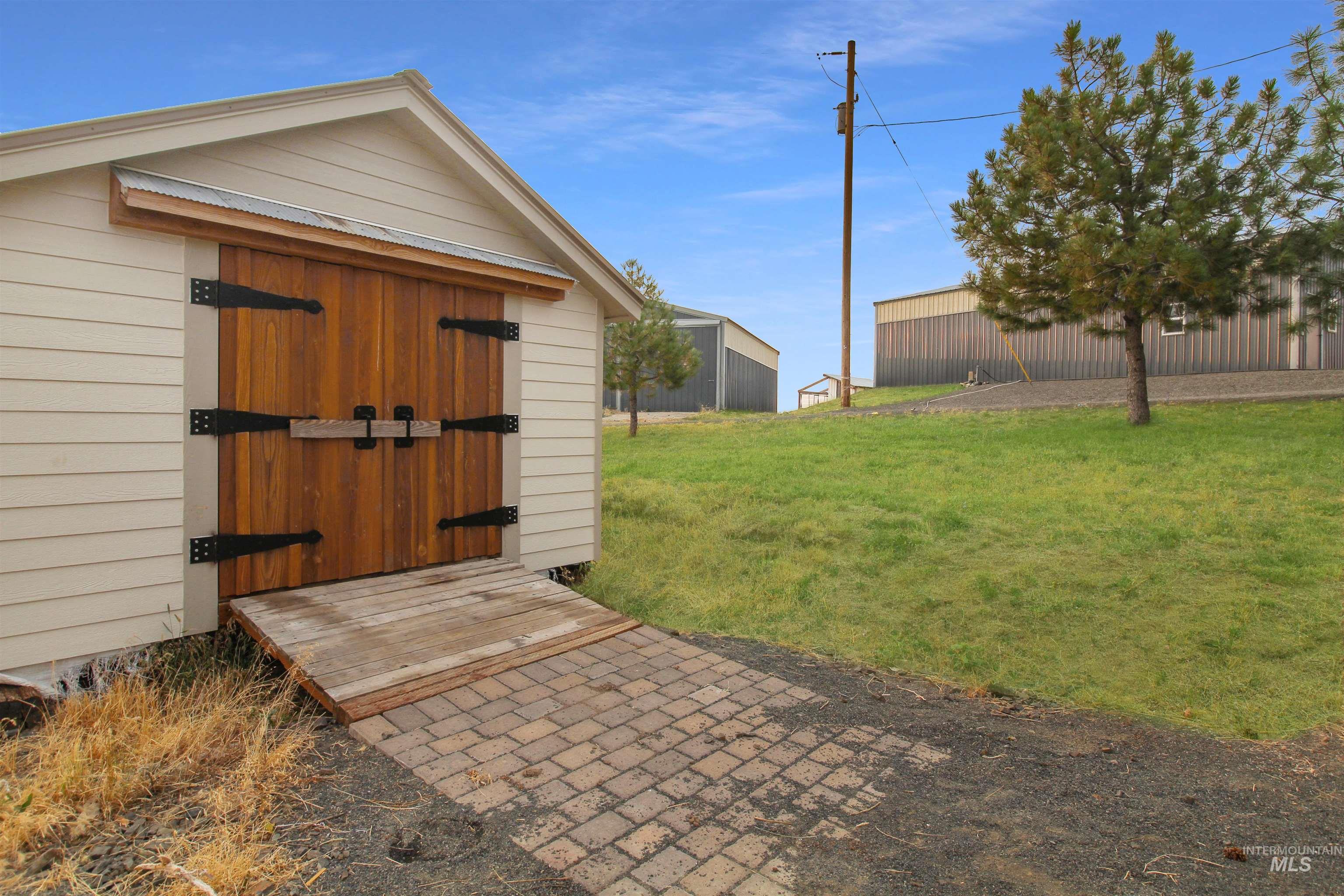 2469 Hague Road Midvale, ID 83645 - Photo 38 of 50 Outbuilding featuring wood panel doors with black hardware, an accompanying wooden ramp, and a brick paver pathway