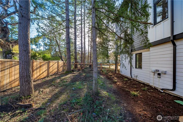 a view of a backyard with large trees and wooden fence