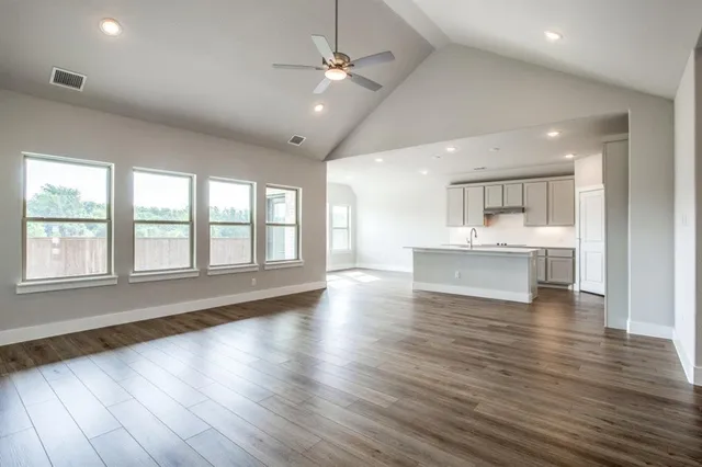 a view of an empty room with wooden floor and a kitchen