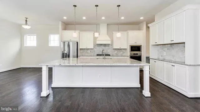 a large white kitchen with kitchen island a sink wooden floor and white cabinets