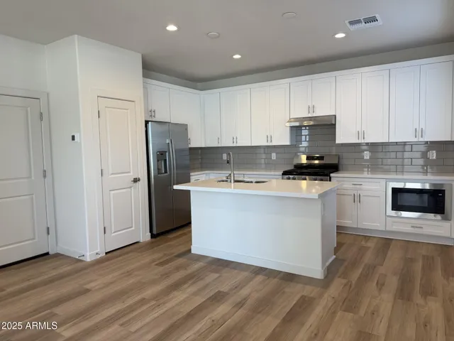 a kitchen with stainless steel appliances a refrigerator stove a sink and white cabinets