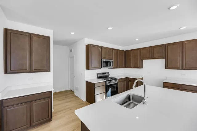 a kitchen with stainless steel appliances a stove top oven a sink a refrigerator white cabinets and wooden floor