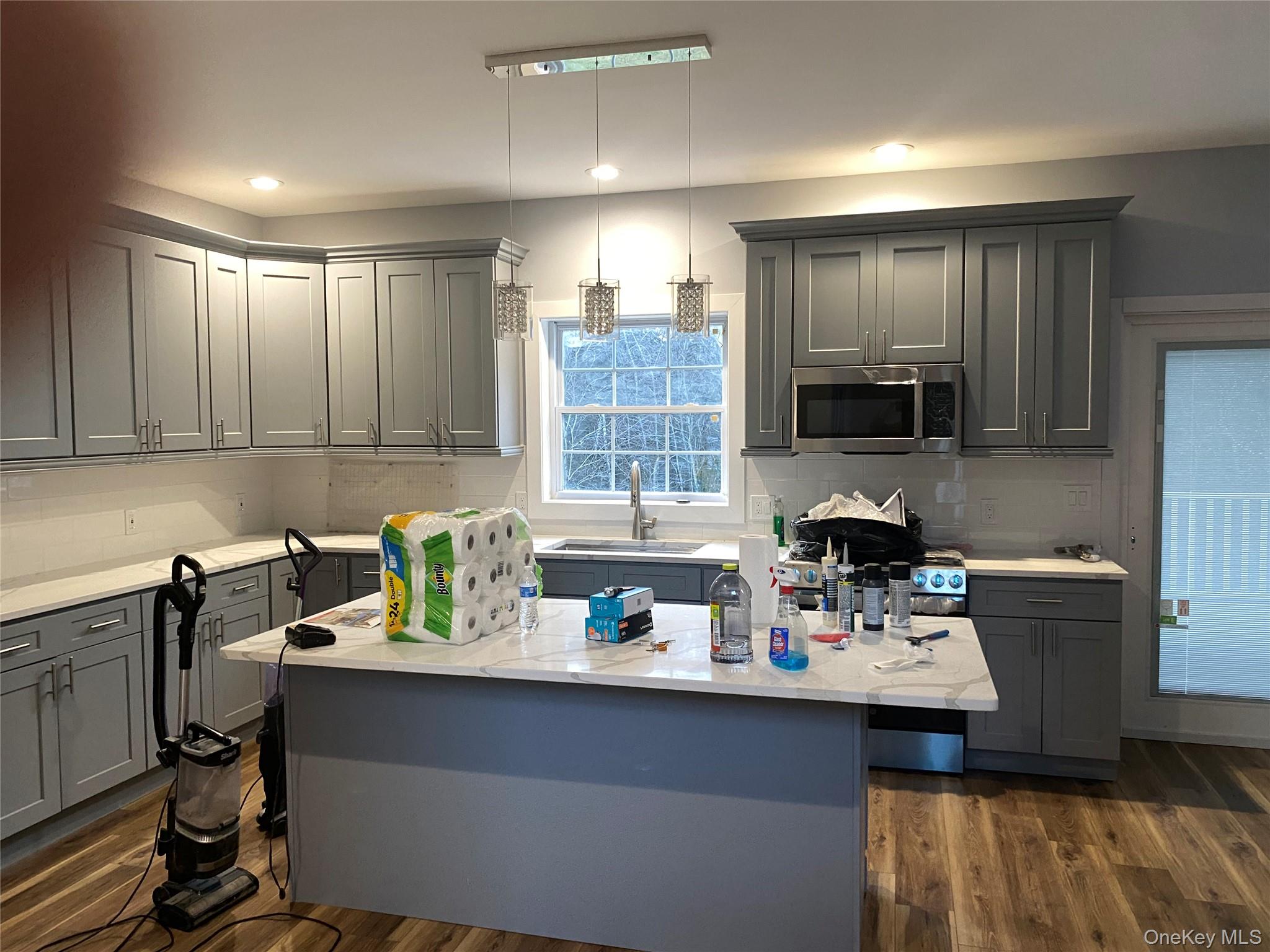 44 Roslyn Ridge Road Mongaup Valley, NY 12762 - Photo 9 of 24 Kitchen featuring gray cabinetry, a center island with sink, stainless steel microwave, hanging light fixtures, and light stone counters