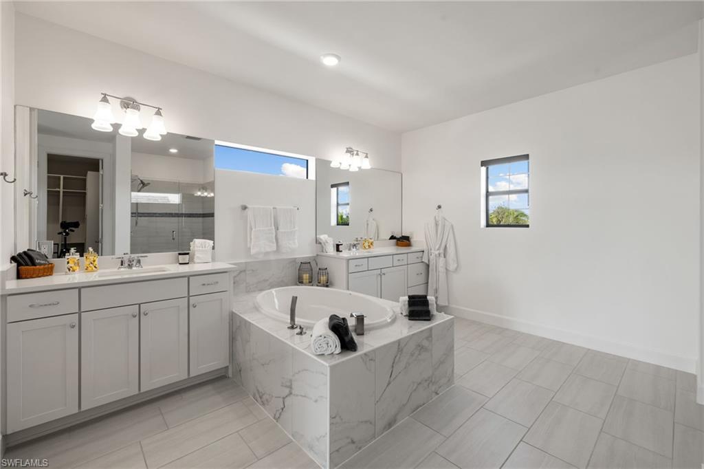 19824 Beverly Park Road Estero, FL 33928 - Photo 27 of 50 Bathroom featuring a shower stall, two vanities, a bath, and plenty of natural light