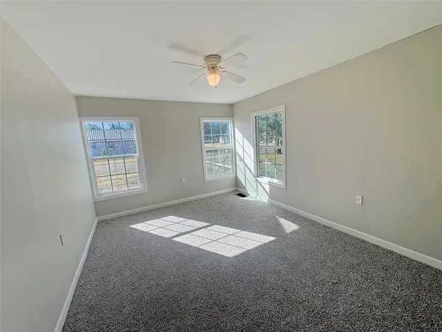 an empty room with windows and ceiling fan