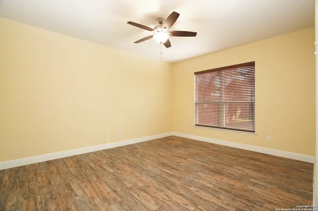 a view of an empty room with wooden floor and a ceiling fan