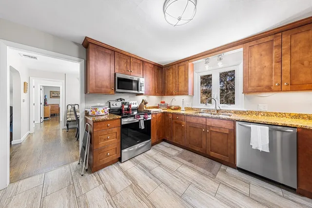 a kitchen with stainless steel appliances granite countertop a stove top oven a sink dishwasher a dining table and chairs with wooden floor