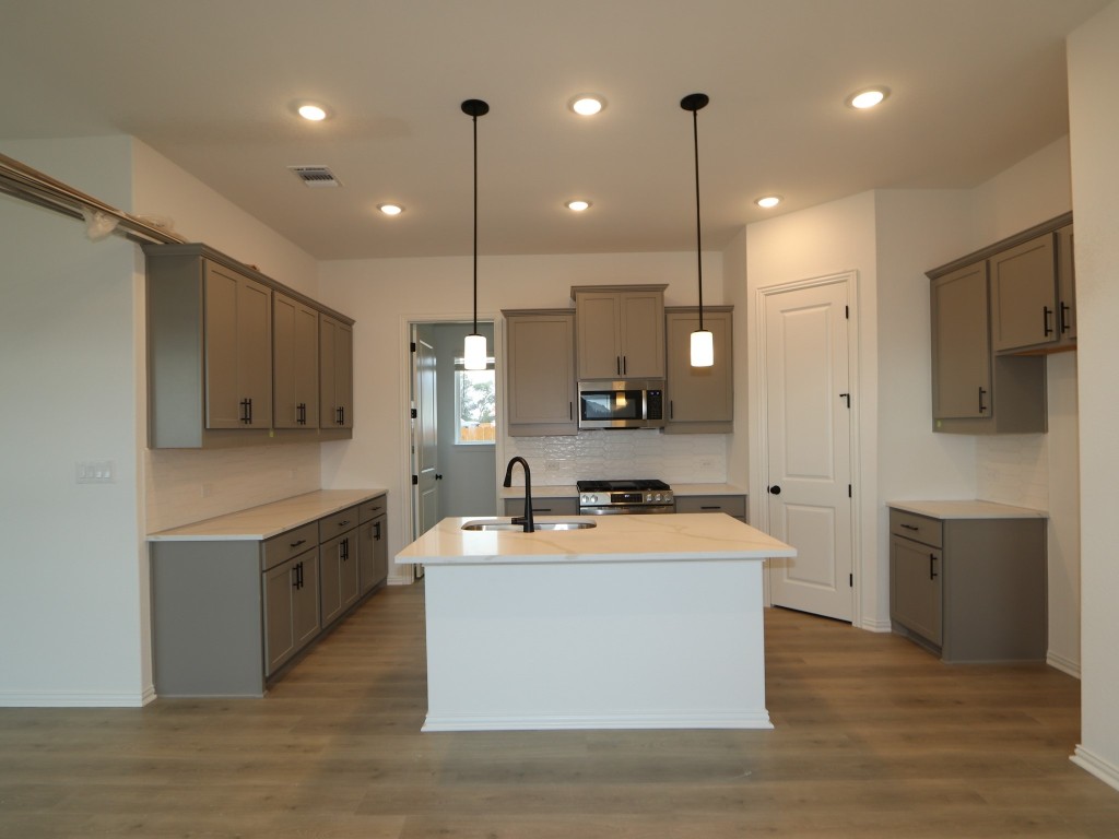 226 Grayson Elm Pass Dripping Springs, TX 78620 - Photo 7 of 23 a large kitchen with kitchen island a stove a sink a center island and wooden floor