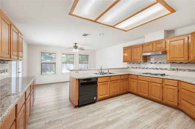 a large kitchen with granite countertop a stove top oven a sink a dining table and chairs with wooden floor