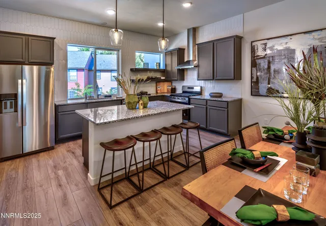 a kitchen with stainless steel appliances kitchen island granite countertop a refrigerator a stove top oven a sink dishwasher and dining table with wooden floor
