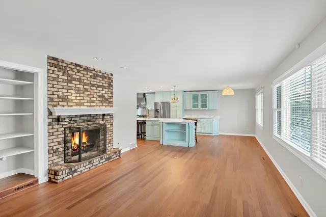 a view of an empty room with wooden floor fireplace and a window