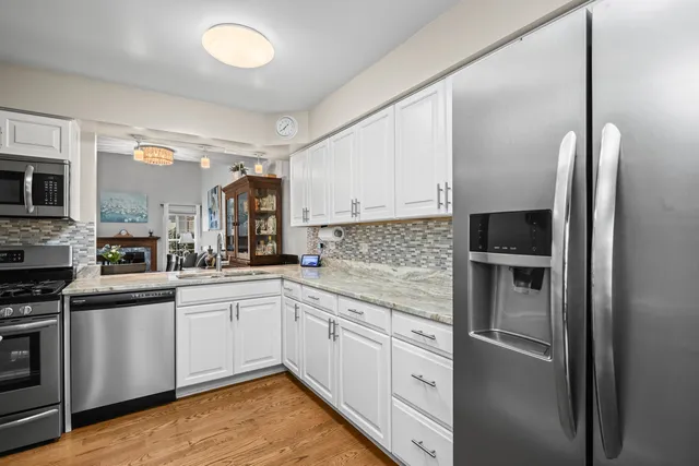 a kitchen with stainless steel appliances granite countertop a refrigerator a stove and a sink with wooden floor