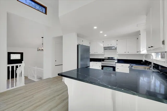 a kitchen with stainless steel appliances granite countertop a refrigerator a stove a sink a microwave a dining table and chairs with wooden floor