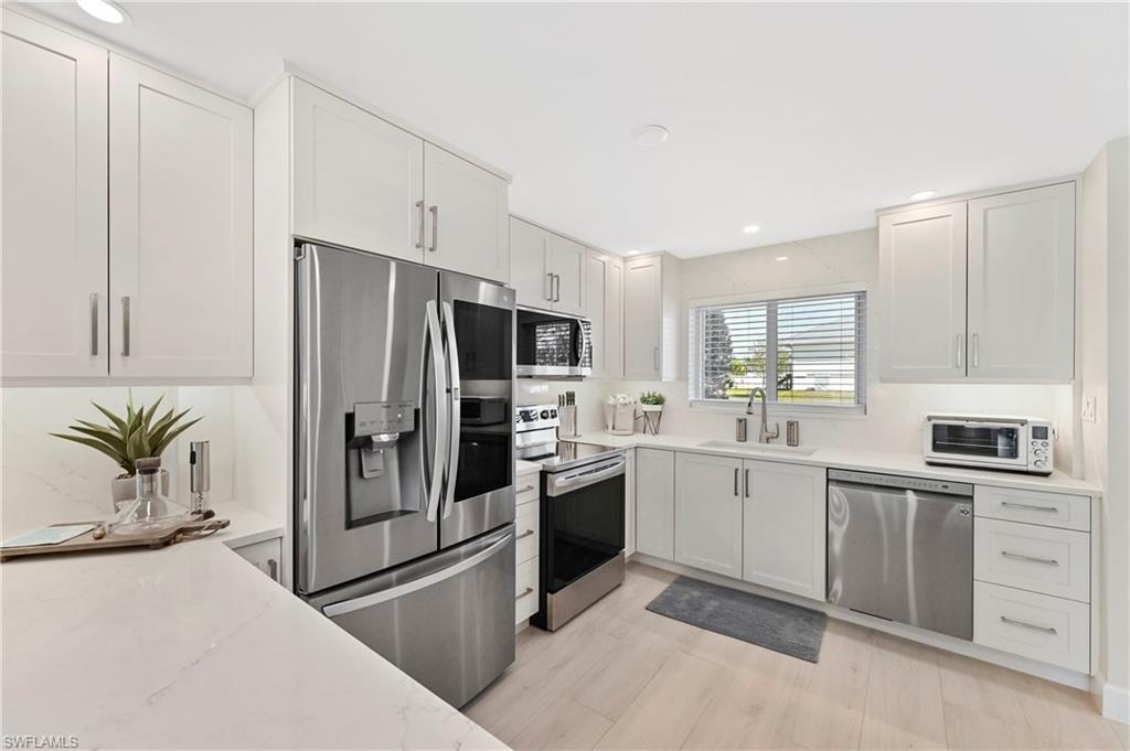 1686 Blue Point Avenue, Unit B5 Naples, FL 34102 - Photo 5 of 46 a kitchen with white cabinets and stainless steel appliances