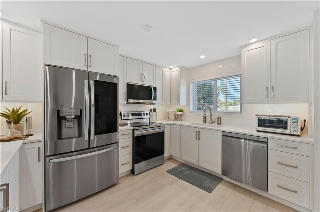 1686 Blue Point Avenue, Unit B5 Naples, FL 34102 - Photo 7 of 46 a kitchen with white cabinets and stainless steel appliances